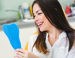 Happy dental patient looking at her smile in mirror